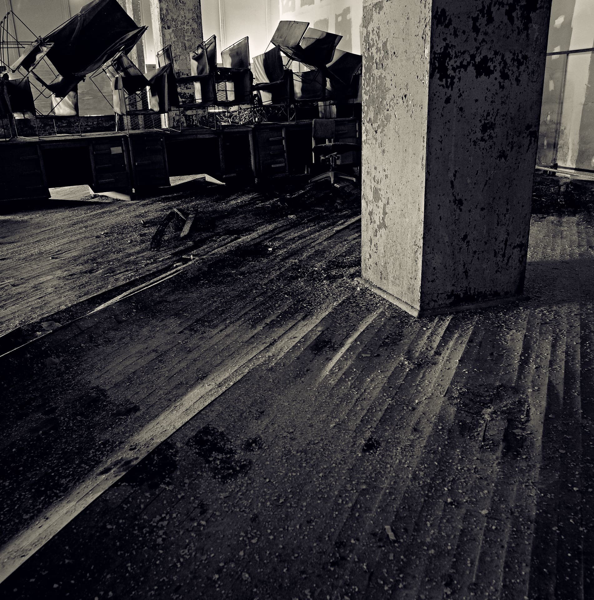Overturned office chairs and desks beyond a concrete column in a gutted floor covered in grit and debris