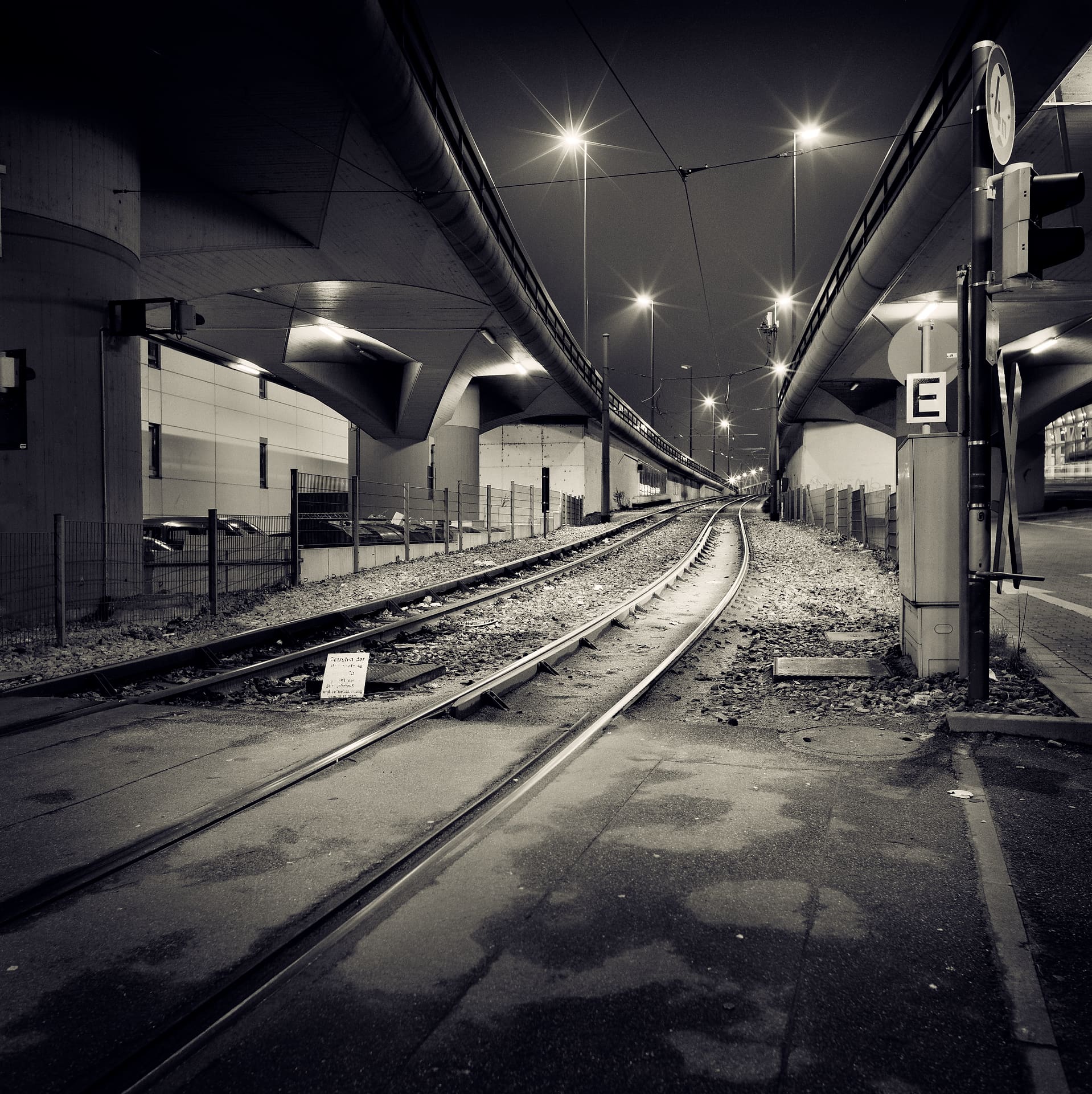 Tram rails curving beneath concrete flyovers at night, streetlamps flaring into stars above wet asphalt