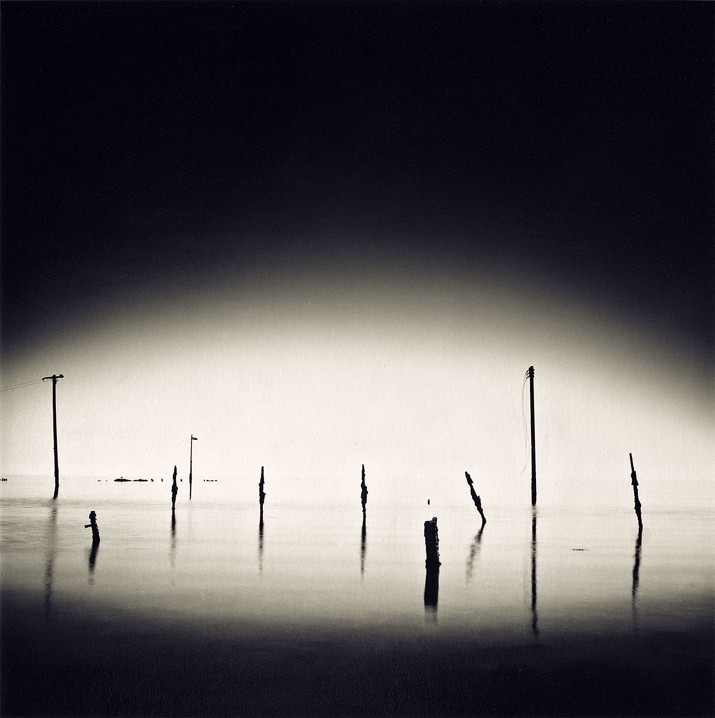 Broken posts and a leaning telephone pole rising from motionless flooded ground, reflections held by long exposure