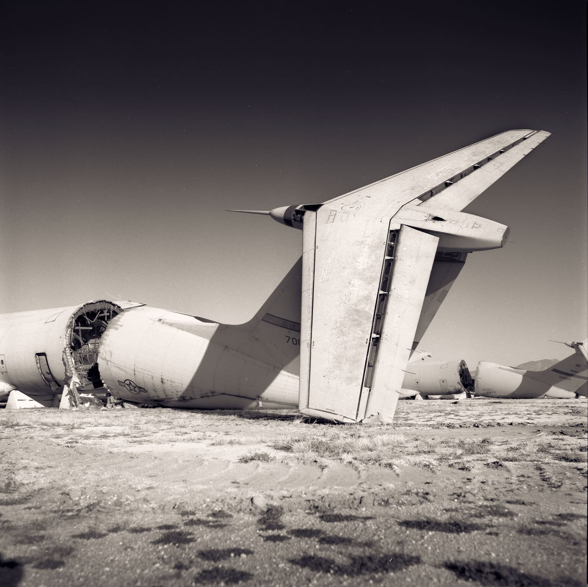 Gutted military transport aircraft with severed fuselage and towering tail fin on dry desert ground, more wrecks behind