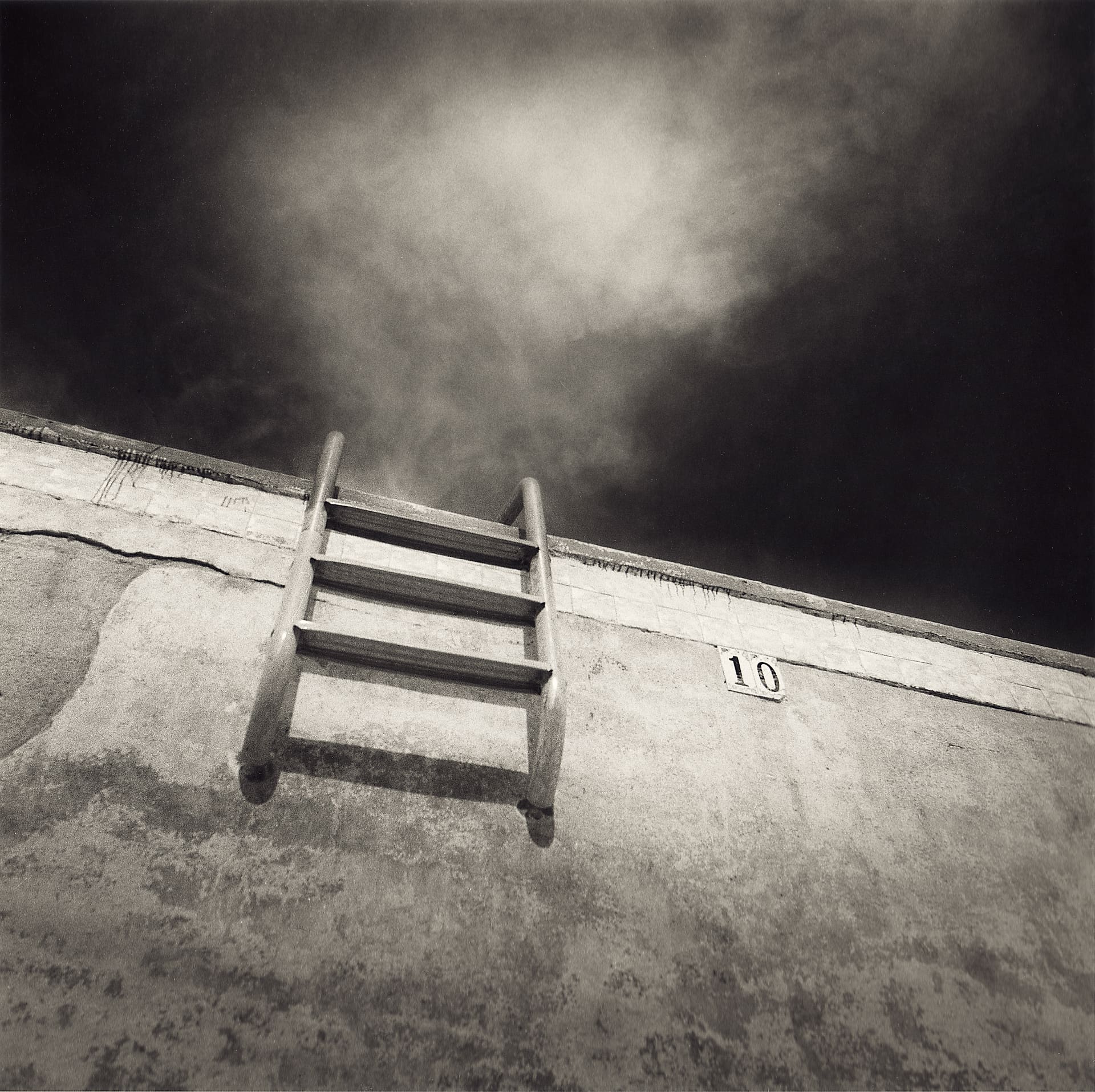 Steeply angled view up a cracked empty swimming pool wall, ladder and painted depth marker ten