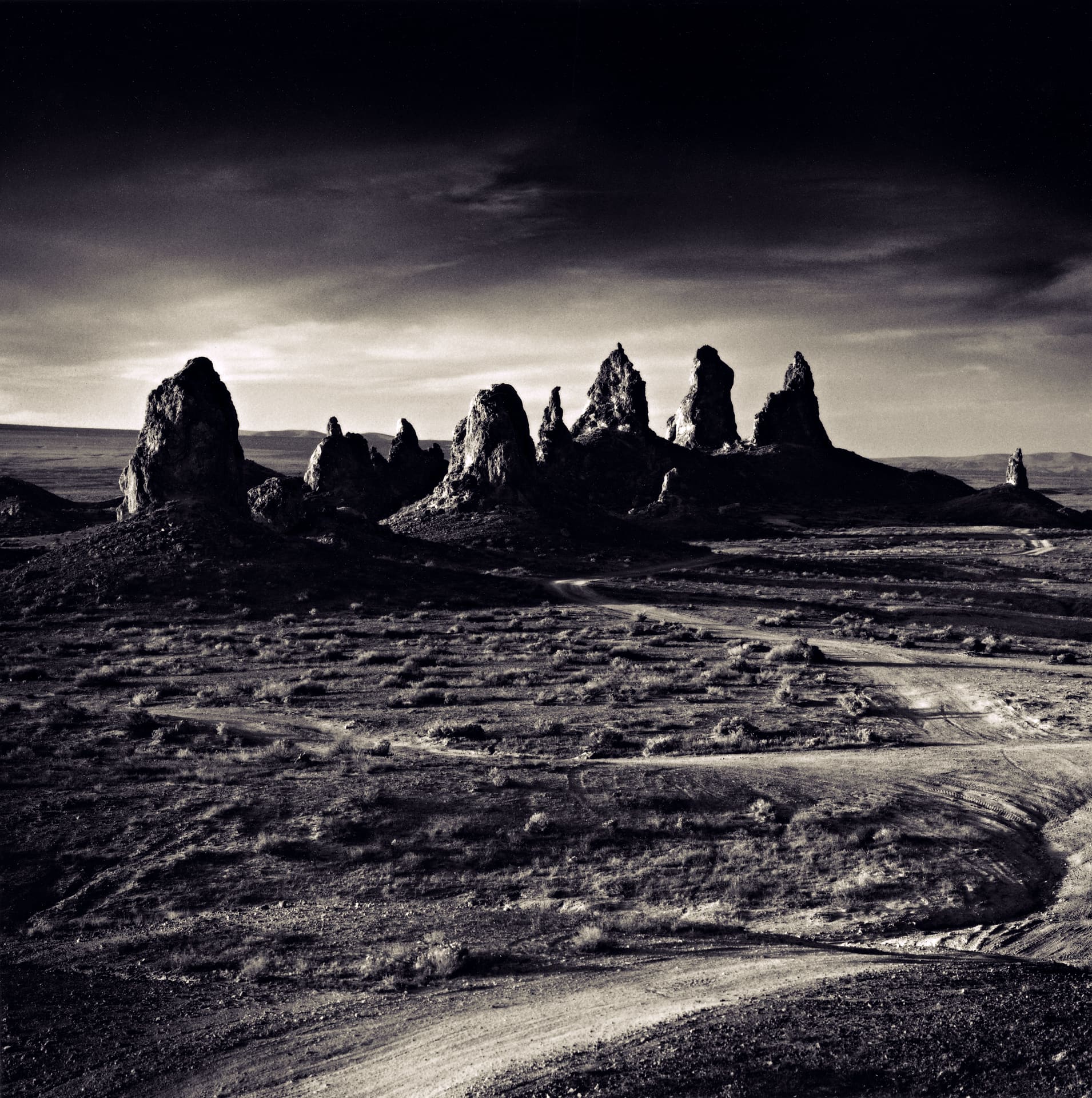 Cluster of jagged tufa spires on a dark desert flat, dirt tracks curving through scrub in foreground